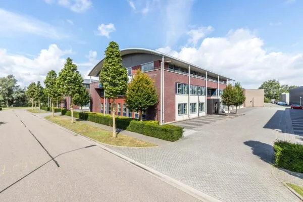 Modern kantoorgebouw aan de straat De Wel met omliggend groen en parkeerplaatsen.